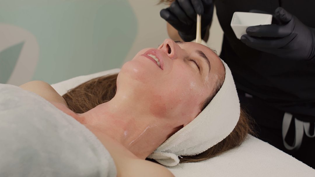 A professional preparing a facial treatment for a relaxed client