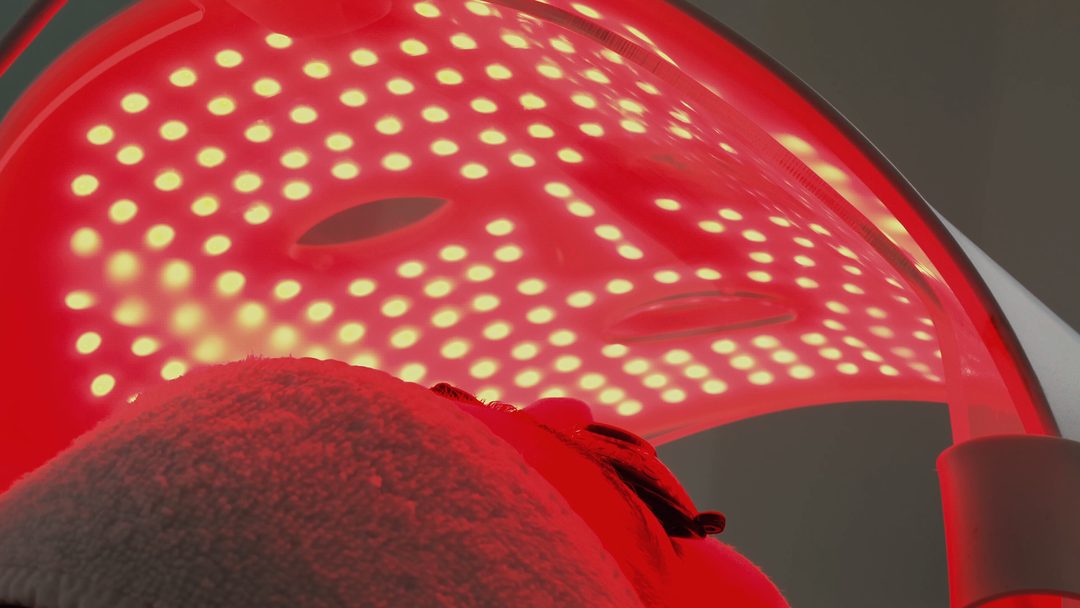 A red LED light panel positioned over a client’s face