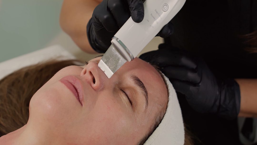 An esthetician using a smooth skincare tool on a client’s face
