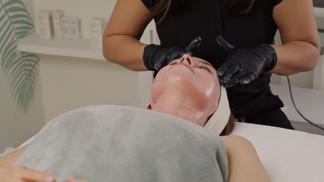 Hands performing a facial massage on a client with closed eyes